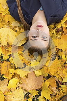 Attractive girl in autumn Park laying on yellow leaves.