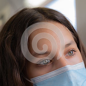 Attractive girl with grey eyes wearing a surgical mask half face closeup shot