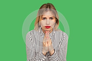 Attractive girl with beautiful red lips and in striped blouse holding hands together, praying to camera