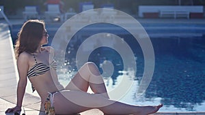 Attractive girl in bikini sitting by swimming pool at resort