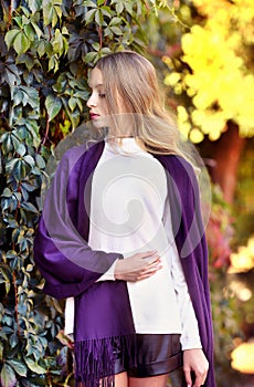 Attractive girl, blond hair in a lilac cape sitting in a botanical garden