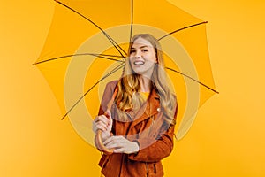 An attractive girl, in a bright yellow dress and an autumn jacket, stands with a yellow umbrella on a yellow background. Autumn