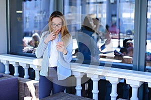 Attractive girl browsing by phone and standing at cafe.