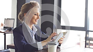 Attractive girl in business suit uses tablet sitting in coffee shop. Business lady is developing a new strategy for the