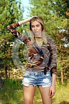 Attractive girl in camo shirt, jeans shorts with backpack on hiking trail in forest