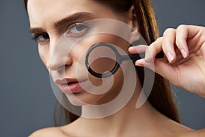 Attractive girl demonstrating perfect skin through magnifying glass