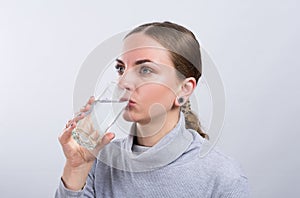 Attractive girl drinking water on light background