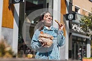 attractive girl eating with big pleasure tasty food from take away cafe in the street. you deserve it