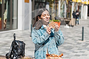attractive girl eating with big pleasure tasty food from take away cafe in the street. you deserve it