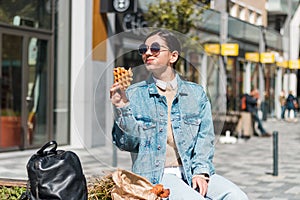 attractive girl eating with big pleasure tasty food from take away cafe in the street. you deserve it