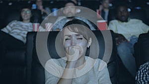 Attractive girl feeling scared during horror film in dark modern cinema