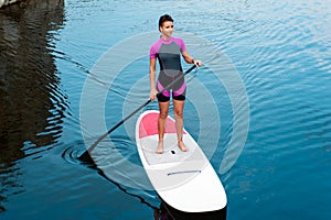 Attractive girl with fit body surfing on stand up paddle board