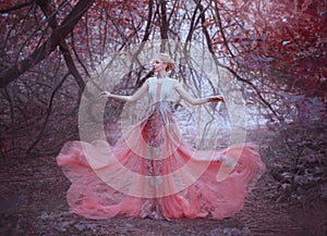 Attractive girl with gorgeous blond hairdo in the forest near the branches of trees, dressed in a light amazing pink