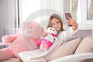 Attractive girl  has fun at home with her favorite soft toys. She taks a selfie on the phone with soft toys