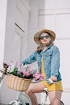 attractive girl in hat sunglasses and denim jacket looking at camera and riding bicycle