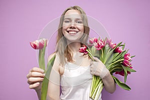 Attractive girl holds a bouquet of flowers on a pink background and gives one tulip, the seller offers flowers, a woman gives