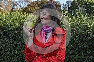 Attractive girl holds fresh green apple in her hand standing in the autumn park