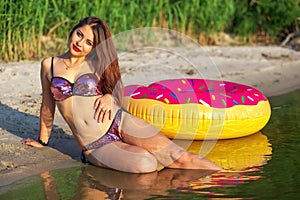 Attractive girl lying on the seashore with inflatable donut. Rest on the beach