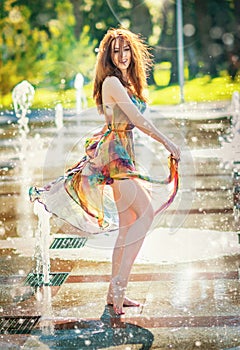 Attractive girl in multicolored short dress playing with water in a summer hottest day. Girl with wet dress enjoying fountains