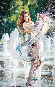 Attractive girl in multicolored short dress playing with water in a summer hottest day. Girl with wet dress enjoying fountains