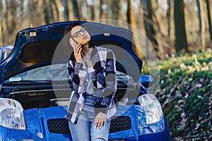 attractive girl with phone near open hood of car