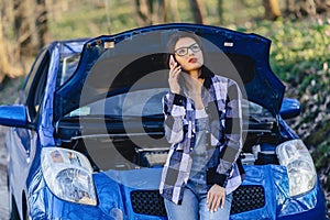attractive girl with phone near open hood of car