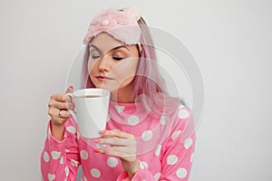 Attractive girl in pink pajamas and sleep mask enjoying her morning coffee