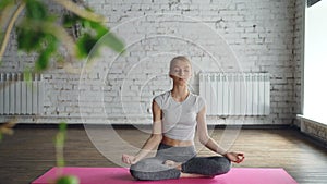 Attractive girl is practicing yoga bending to side with arm up then relaxing in easy lotus pose on individual session in