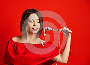 Attractive girl in red dress holding a fork in hands. on the headphone plug. prepared to eat.