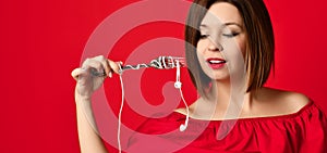 Attractive girl in red dress holding a fork in hands. on the headphone plug. prepared to eat