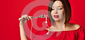 Attractive girl in red dress holding a fork in hands. on the headphone plug. prepared to eat.