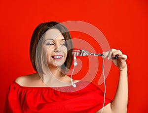 Attractive girl in red dress holding a fork in hands. on the headphone plug. prepared to eat.