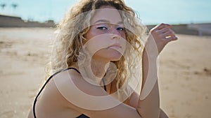 Attractive girl resting sea shore looking camera close up. Woman sitting sand