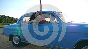 Attractive girl in sunglasses leaning out of vintage car window and enjoying trip. Young couple travel on retro car in