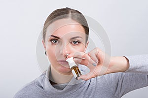 Attractive girl taking a medicine with spray inside the nose on light background