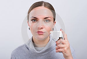 Attractive girl taking a medicine with spray inside the throat on light background