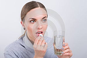 Attractive girl taking a pill with water on light background