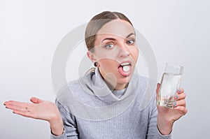 Attractive girl taking a pill with water on light background