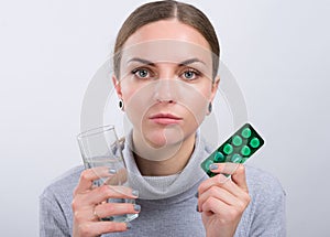 Attractive girl taking a pills with water on light background