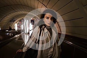 Attractive girl in trench coat intently looking in camera on escalator at subway station