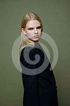 An attractive girl turns into the camera from behind her shoulder. Cool model posing on a green background in the studio