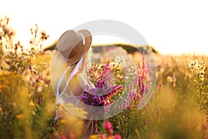 Attractive girl walking in field, meadow with grass and flowers in the sunset