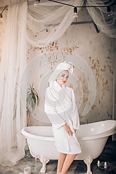 Attractive girl wearing white bathrobe and towel on head in bathroom