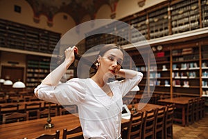 Attractive girl in a white blouse poses for the camera in the old atmospheric public library