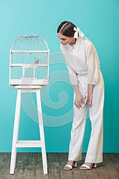 attractive girl in white looking at parrot in cage