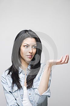 Attractive girl woman with long black hair palms up showing something over a grey background.