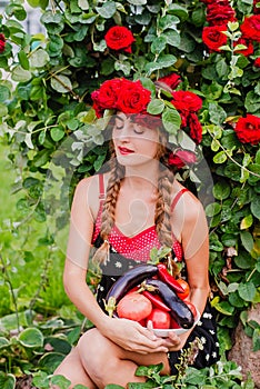 Attractive girl with a wreath of red roses with a basket of vegetables: tomatoes, eggplants, peppers