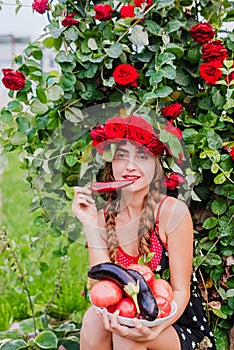 Attractive girl with a wreath of red roses with a basket of vegetables: tomatoes, eggplants, peppers