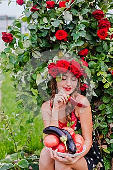 Attractive girl with a wreath of red roses with a basket of vegetables: tomatoes, eggplants, peppers