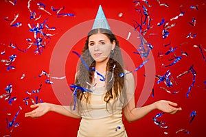 Girl in a yellow T-shirt and in a festive cap throws blue and silver confetti.